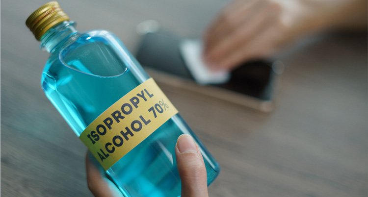 A bottle of isopropyl alchohol and a hand cleaning a phone on the background