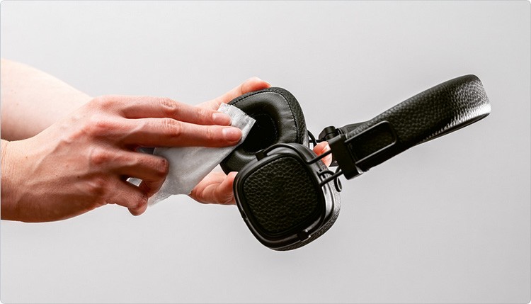 A man cleans headphones with a wet tissue