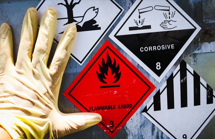 A gloved hand pointing at hazard signs, including a flammable warning